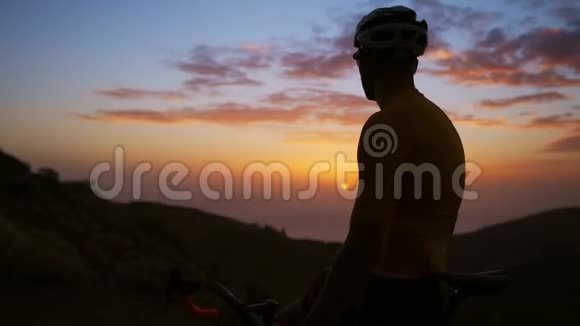 骑自行车的人站在山顶欣赏日落相机在Stadicam上移动视频的预览图
