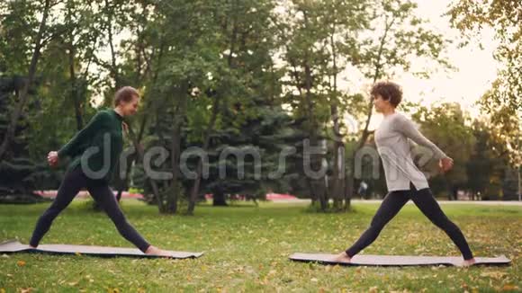 瑜伽学生在户外锻炼教练伸展双腿背部向前弯曲站在绿色的垫子上视频的预览图