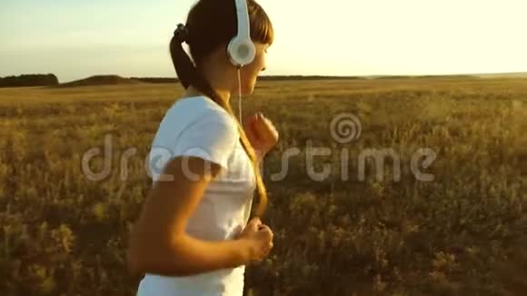 戴着耳机的女孩沿着路跑美丽的女孩在日落时分在农村做体育锻炼视频的预览图