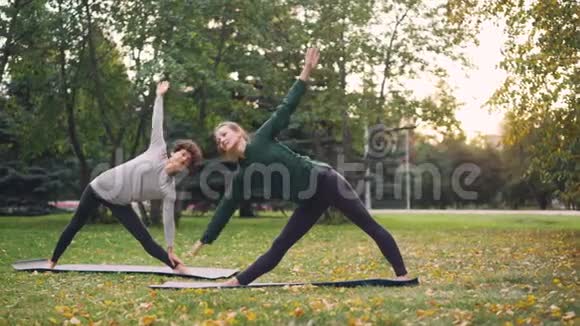 有经验的教师苗条的女孩在城市公园温暖的秋日教她的女学生瑜伽体式视频的预览图