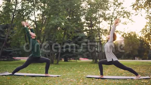 迷人的女孩正在公园里享受户外瑜伽练习姿势站在垫子上老师在讲话视频的预览图