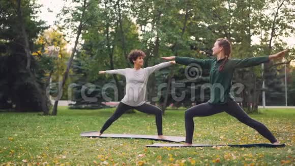 两位美丽的女孩瑜伽老师和学生正在公园里练习站立在垫子上和移动身体的体式序列视频的预览图