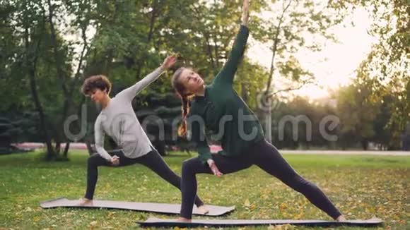 两个漂亮的女人在公园里做瑜伽在垫子上练习体式和呼吸新鲜空气个别做法视频的预览图