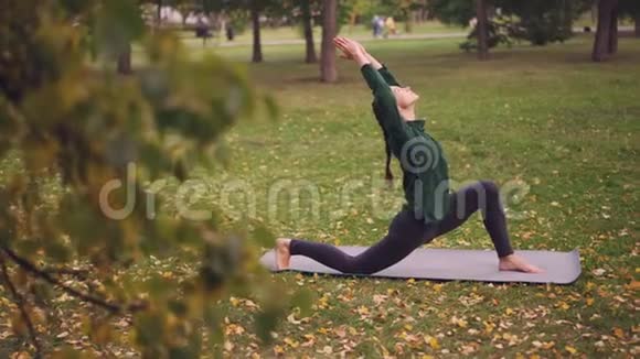 漂亮的年轻女士正在公园里进行户外瑜伽练习她正在垫子上做运动享受新鲜的活动视频的预览图