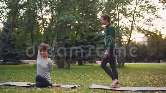 斯利姆女孩瑜伽教练正在帮助她的学生在秋季公园的个人练习中管理Gomukhasana视频的预览图
