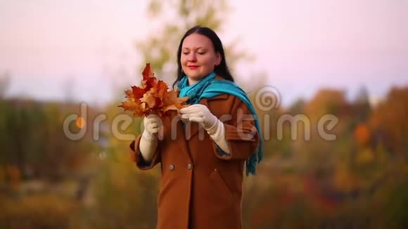 秋天公园里的年轻微笑的女人手里拿着一束枫叶慢动作视频的预览图