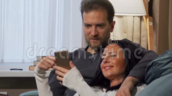 美丽的女人在她的智能手机上向丈夫展示一些有趣的东西视频的预览图