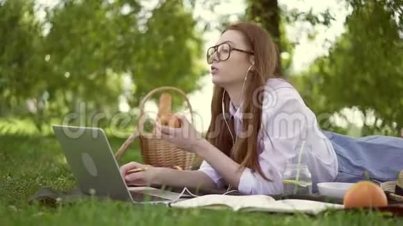 干姜女用笔记本电脑躺在公园里吃苹果视频的预览图