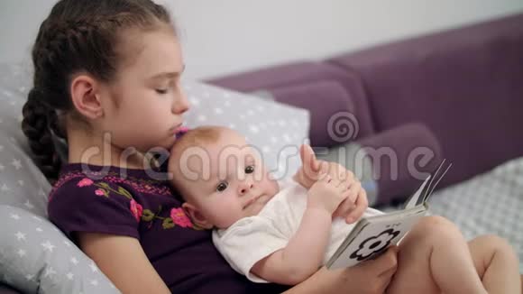 漂亮的女孩在家和宝宝一起读童书妹妹抱着宝贝弟弟视频的预览图