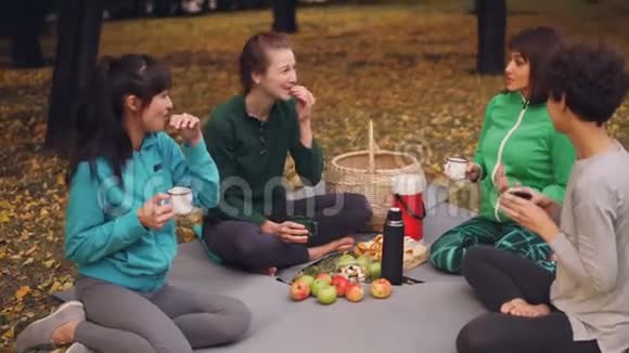 漂亮的女运动员在户外训练后放松在垫子上野餐吃零食喝茶女孩视频的预览图