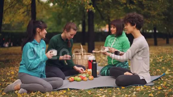 快乐的女孩在公园里野餐坐在瑜伽垫上在秋天的户外练习后吃东西女孩们视频的预览图