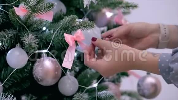 年轻女子的双手在圣诞树上展开一个蝴蝶结用节日的灯光和视频的预览图