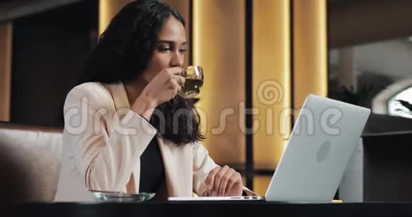 年轻的商务女性在笔记本电脑上看在线课程她坐在咖啡馆里喝茶视频的预览图