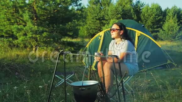 一个戴墨镜的女人在炉火旁喝茶欣赏大自然视频的预览图