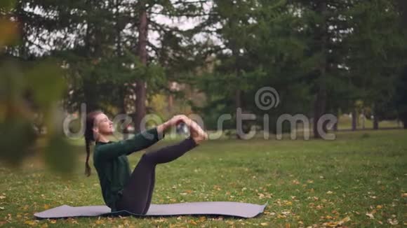 微笑的年轻女子在公园里锻炼身体在草地上坐着瑜伽享受新鲜的空气视频的预览图