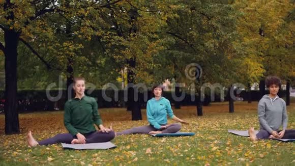 周末漂亮的女运动员们坐在城市公园的瑜伽垫上做伸展运动休闲活动视频的预览图