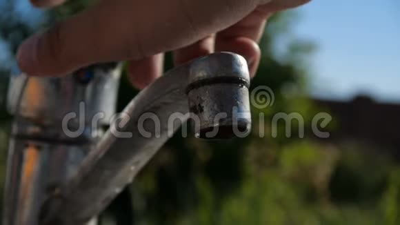 女人的手在花园里打开一个金属的水龙头在邋遢的塞莱斯特天空中视频的预览图