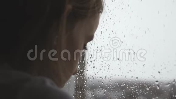 伤心的少年女孩在雨天透过窗户看着外面视频的预览图