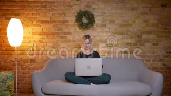 年轻漂亮金发女性的特写镜头她使用笔记本电脑坐在舒适的家里的沙发上视频的预览图