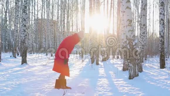 穿着红色冬衣穿着毛毡靴的漂亮年轻女子带着桦树漫步在画报城市公园扔雪视频的预览图
