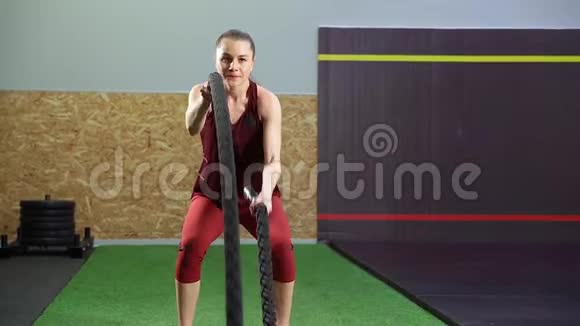 年轻的成年女孩在健身房进行交叉健身锻炼时练习战绳锻炼视频的预览图