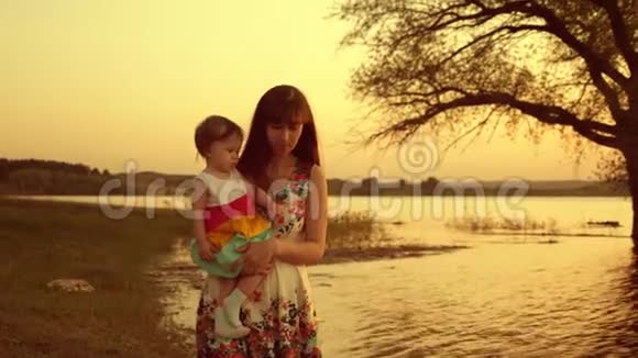 日落时分妈妈和女儿正沿着湖边的海滩散步妈妈怀里的快乐孩子视频的预览图