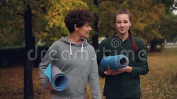 多莉拍摄的女性朋友瑜伽健将在公园里散步手提瑜伽垫说话时享受新鲜空气和交谈视频的预览图