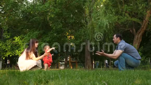 爸爸妈妈学着走路孩子夏天在公园的草坪上迈出第一步视频的预览图