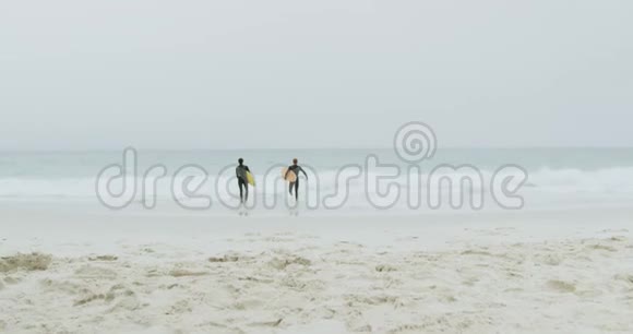 两名男性冲浪者与冲浪板一起在海滩上奔跑的后视图视频的预览图