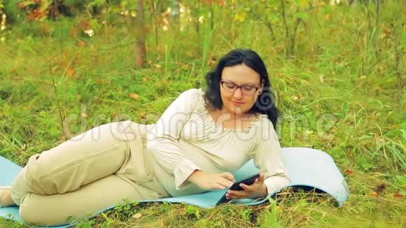 森林里一个戴着眼镜的年轻活泼的女人躺在地毯上做瑜伽用信使传递信息视频的预览图