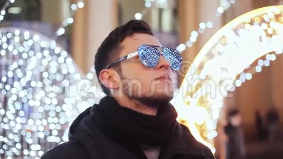 时尚的男人在庆祝新年城市圣诞树花环和灯光反射在镜子太阳镜上视频的预览图