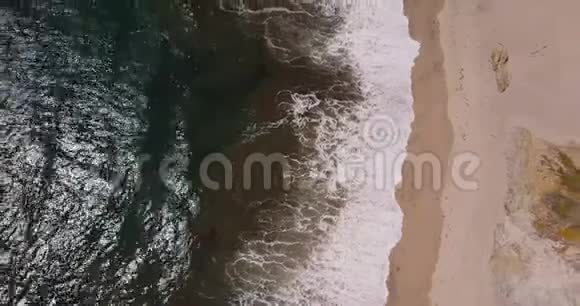 空中俯视放大拍摄美丽的泡沫海浪到达阳光明媚的异国沙滩在大南加州视频的预览图