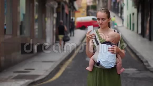 妈妈正站在街上带着一个婴儿吊着吊带为社交网络拍摄了一段关于他去旅行的视频视频的预览图