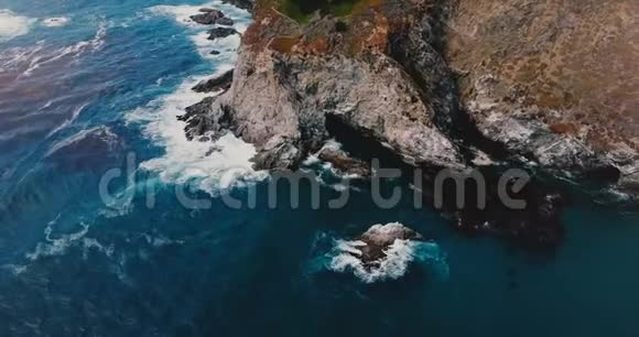 空中俯视无人机拍摄美丽的蓝色海浪撞击阳光下的岩石海岸线在大南加州视频的预览图