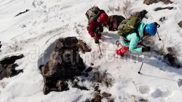 两个穿着全套装备的登山者带着头盔和背包克服了厚厚的积雪和滑滑的岩石爬上了山顶视频的预览图