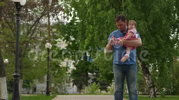 可爱的爸爸把她的女儿穿在夏天的绿色公园里的凉鞋上视频的预览图