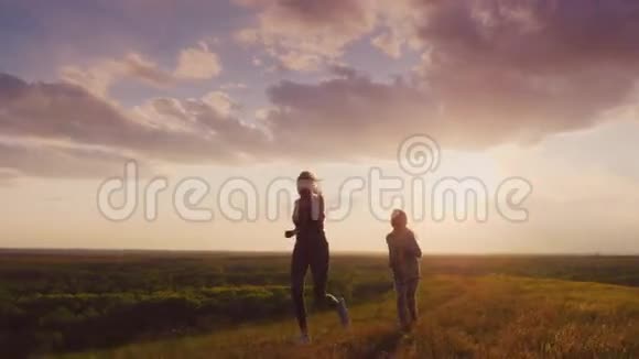 妈妈和女儿在日落时在风景如画的地方跑步积极的生活方式和健康的家庭4K慢动作视频视频的预览图