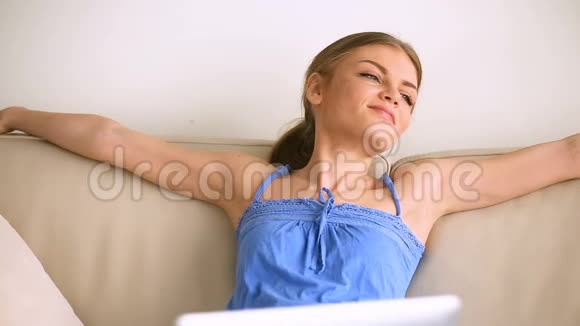 年轻女子坐在沙发上放松享受懒惰呼吸空气视频的预览图