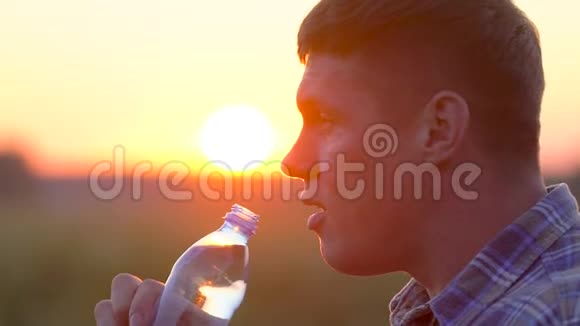 年轻人在麦田里从自然界的塑料瓶里喝清水日落时分在户外休息的男人视频的预览图