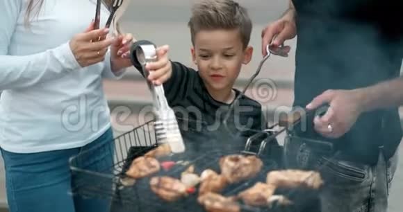 幸福的家庭在烤架上煮肉父亲和母亲带着儿子在烤架上煎香肠微笑着慢动作视频的预览图