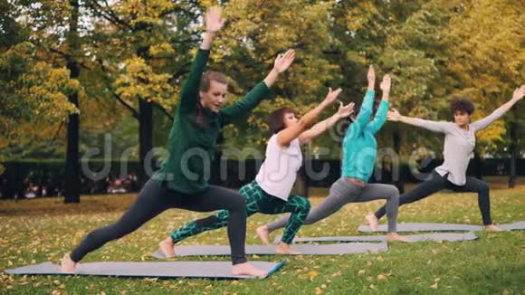 在公园的户外课堂上年轻的女瑜伽学生站在战士的姿势然后移动到三角形的位置视频的预览图