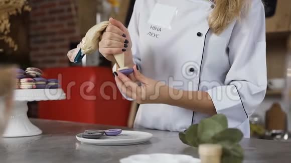 用油酥包将两半的马卡龙与奶油连接起来的厨师手的特写镜头视频的预览图