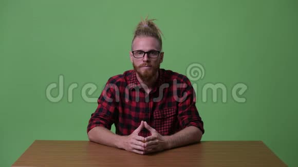 一位英俊的留胡子的嬉皮士正在木桌旁接受采访视频的预览图