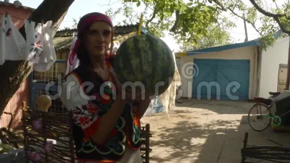 一位身穿乌克兰传统民俗服装的年轻女子在一个农村院子里手里拿着一个大西瓜视频的预览图