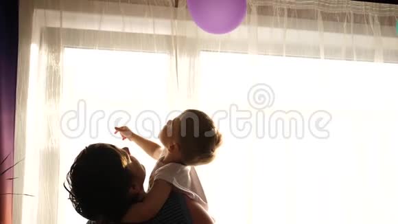 年轻的父亲抱着他的孩子靠近窗户阳光透过窗户孩子的欢笑和喜悦视频的预览图
