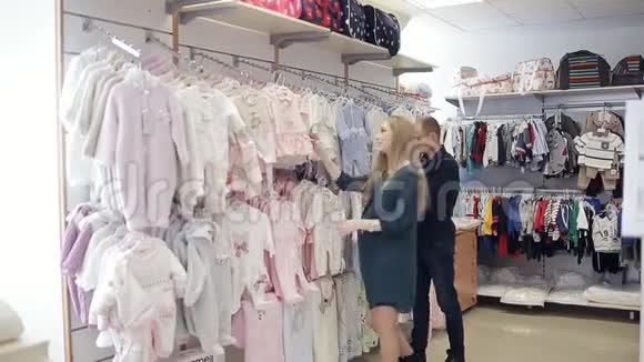 幸福的孕妇和丈夫在一家儿童服装店为婴儿挑选衣服视频的预览图