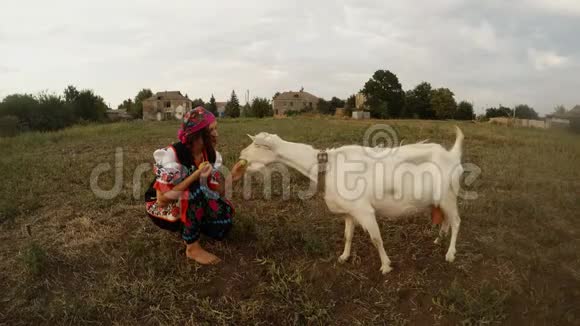 一个穿着乌克兰传统民俗服装的年轻女子自己喂苹果喂白山羊视频的预览图