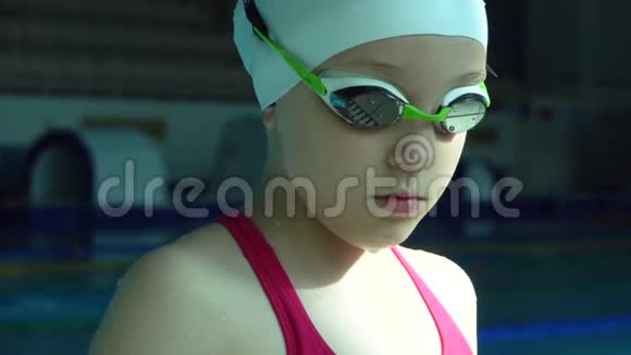 戴着护目镜的少女在游泳池里看着摄像机闭上眼睛视频的预览图