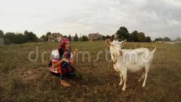 一个穿着传统的乌克兰民俗服装的年轻女人吃一个苹果和一只白山羊视频的预览图