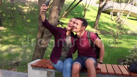 年轻情侣坐在公园长椅上合影留念视频的预览图